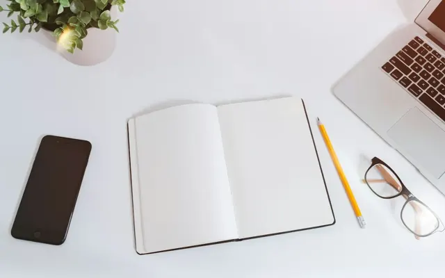 Notebook, phone and laptop on a white desk